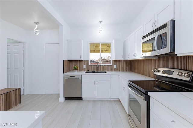 kitchen with light stone counters, appliances with stainless steel finishes, white cabinets, a sink, and light wood-type flooring