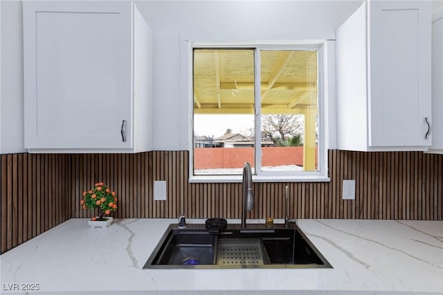details featuring white cabinets, a sink, a wainscoted wall, wooden walls, and light stone countertops