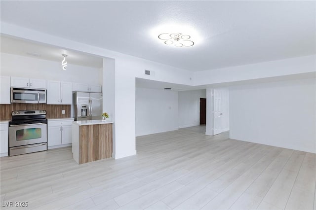 kitchen with light wood finished floors, open floor plan, appliances with stainless steel finishes, and light countertops