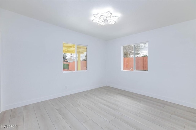 spare room featuring light wood-type flooring, baseboards, and a healthy amount of sunlight