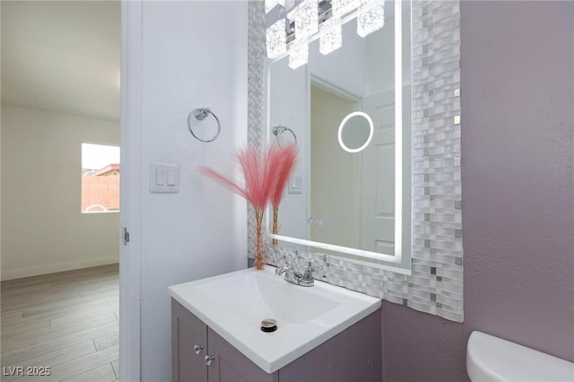 half bath featuring wood finished floors, vanity, toilet, and baseboards