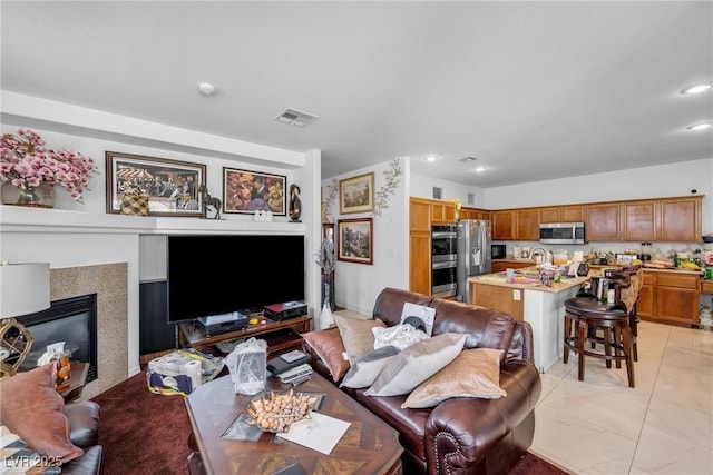 living room featuring a glass covered fireplace, visible vents, light tile patterned flooring, and recessed lighting