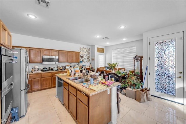 kitchen with stainless steel appliances, visible vents, a sink, and an island with sink