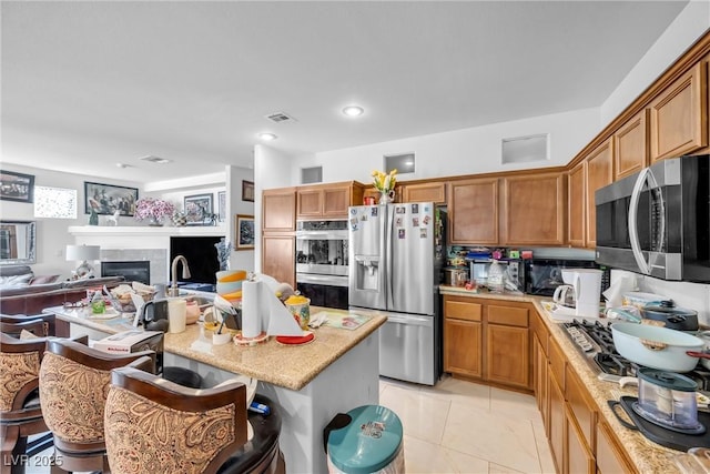 kitchen featuring stainless steel appliances, a glass covered fireplace, open floor plan, and brown cabinets