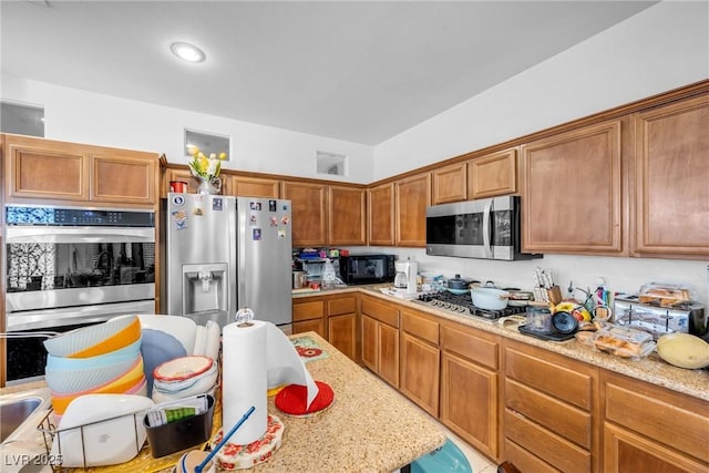 kitchen with appliances with stainless steel finishes, brown cabinetry, and light stone counters