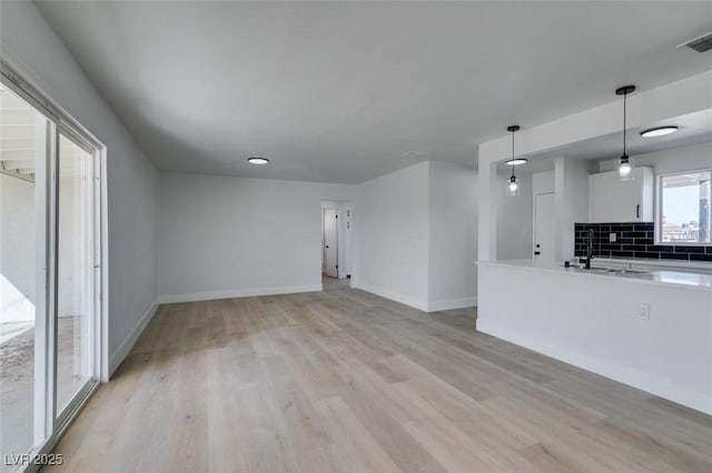 unfurnished living room with light wood-type flooring, a sink, visible vents, and baseboards