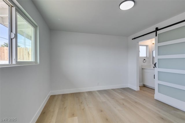 unfurnished bedroom with baseboards, a barn door, multiple windows, and light wood-style floors