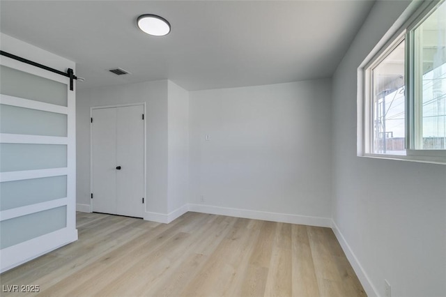 unfurnished room featuring light wood finished floors, a barn door, visible vents, and baseboards