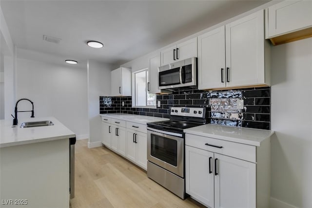 kitchen with decorative backsplash, light wood-style flooring, appliances with stainless steel finishes, light countertops, and a sink