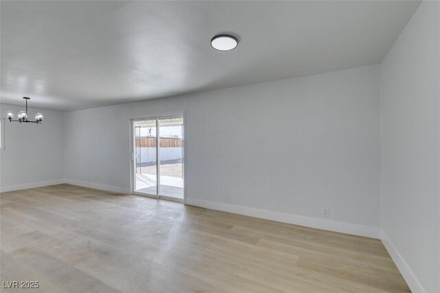 spare room with a notable chandelier, light wood finished floors, and baseboards