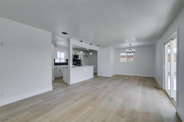 unfurnished living room featuring a chandelier, baseboards, visible vents, and light wood finished floors
