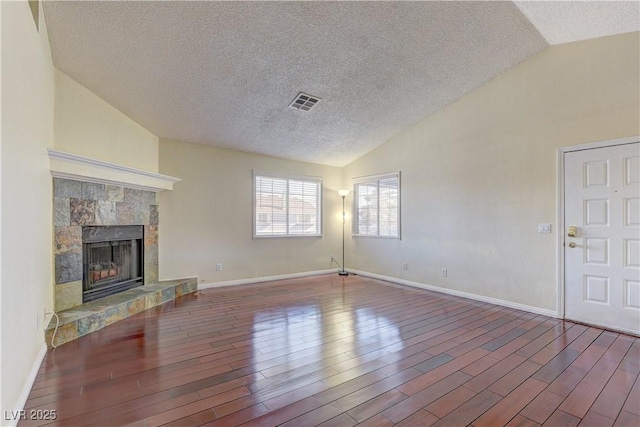 unfurnished living room featuring lofted ceiling, a fireplace with raised hearth, and wood finished floors