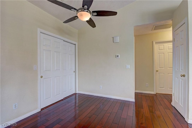 unfurnished bedroom featuring dark wood-style floors, a closet, attic access, a ceiling fan, and baseboards