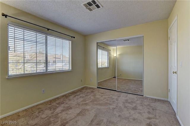 unfurnished bedroom with a textured ceiling, a closet, carpet, and visible vents