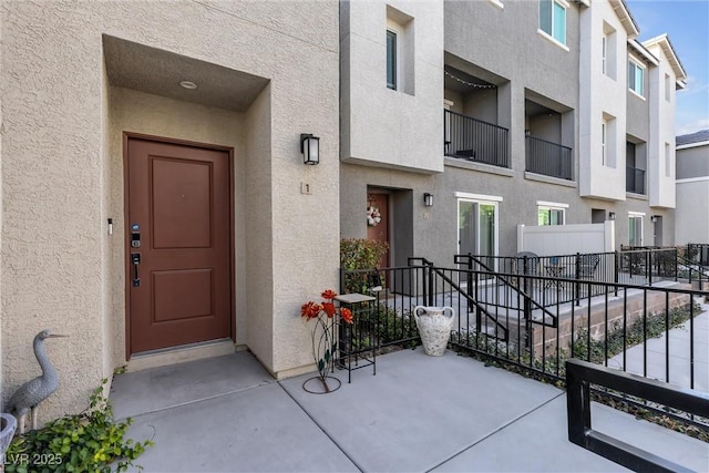 view of exterior entry with fence and stucco siding