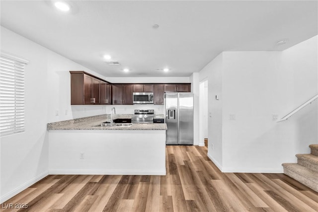 kitchen with stainless steel appliances, light wood finished floors, a sink, and dark brown cabinetry