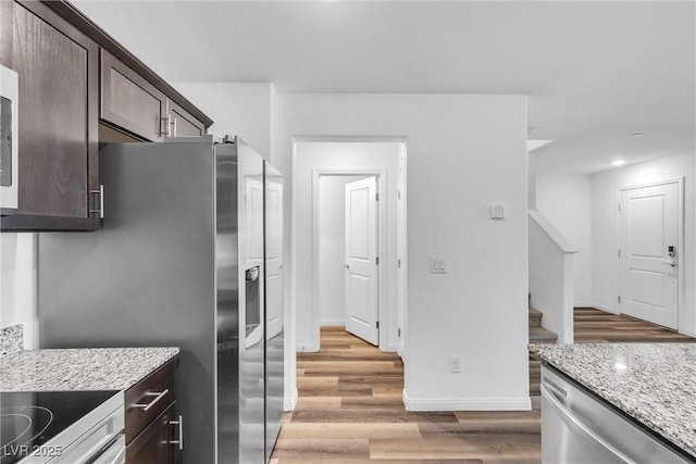 kitchen with dark brown cabinetry, baseboards, light wood-style flooring, appliances with stainless steel finishes, and light stone countertops