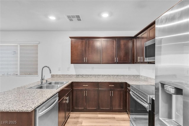 kitchen featuring light stone counters, a peninsula, a sink, visible vents, and appliances with stainless steel finishes