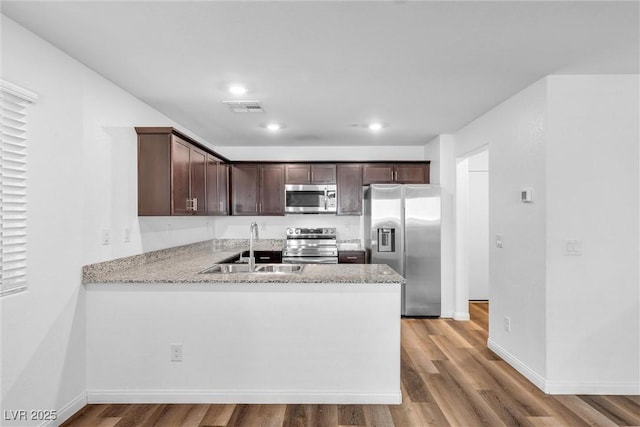 kitchen featuring dark brown cabinetry, a sink, visible vents, appliances with stainless steel finishes, and light wood-type flooring