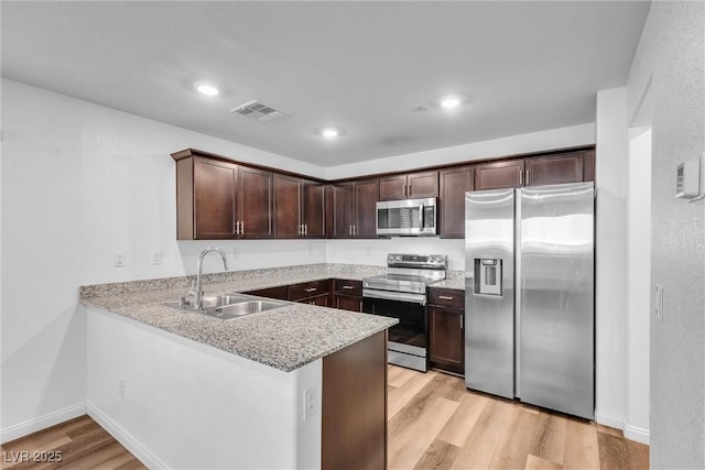 kitchen with light wood-style flooring, appliances with stainless steel finishes, a sink, dark brown cabinets, and a peninsula