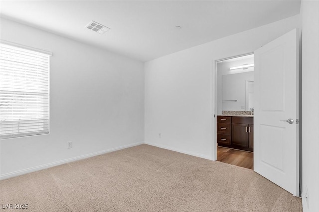 unfurnished bedroom with baseboards, visible vents, ensuite bath, carpet flooring, and a sink