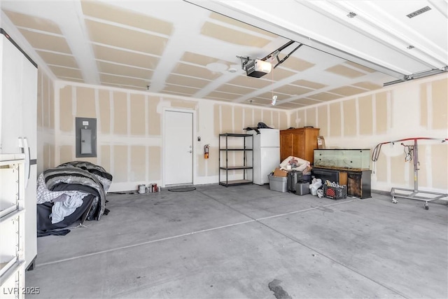 garage featuring visible vents, freestanding refrigerator, electric panel, and a garage door opener