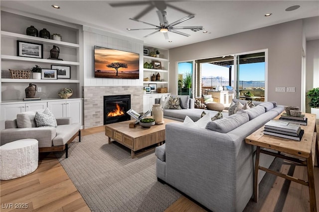 living room with light wood-style floors, built in shelves, a tiled fireplace, and recessed lighting