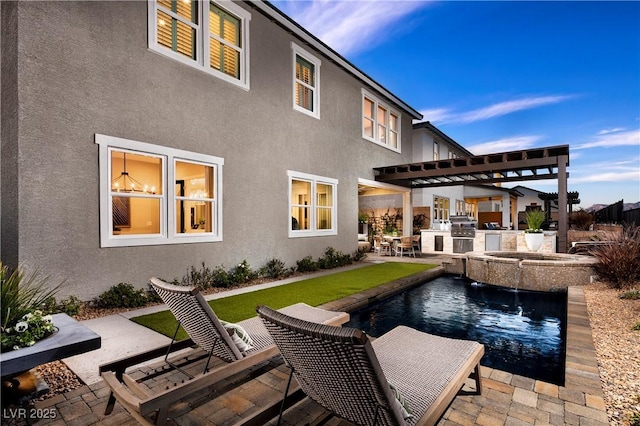 rear view of house featuring an outdoor pool, a patio area, an outdoor kitchen, and stucco siding