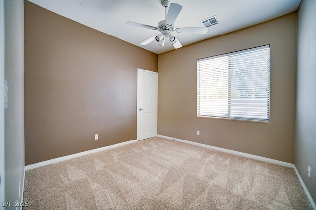 empty room with carpet floors, a ceiling fan, visible vents, and baseboards