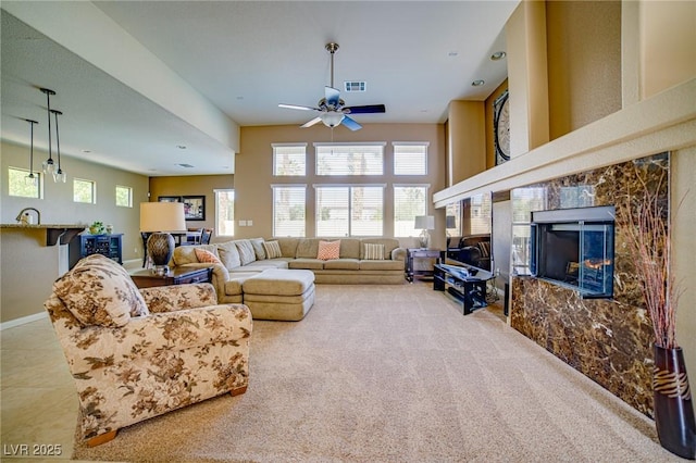 carpeted living area featuring visible vents, a premium fireplace, a ceiling fan, a sink, and baseboards