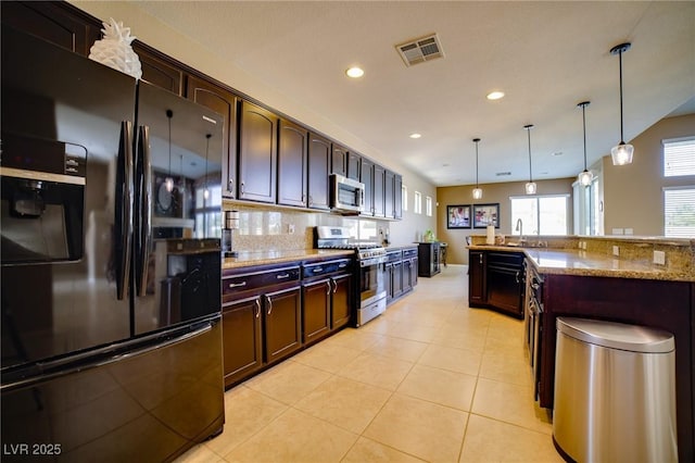 kitchen with light tile patterned floors, tasteful backsplash, appliances with stainless steel finishes, decorative light fixtures, and dark brown cabinets