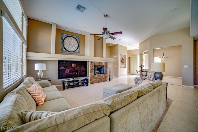 living room featuring light tile patterned floors, visible vents, a high end fireplace, baseboards, and ceiling fan with notable chandelier