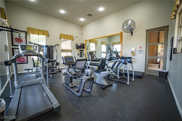 exercise room with a healthy amount of sunlight, visible vents, a towering ceiling, and baseboards