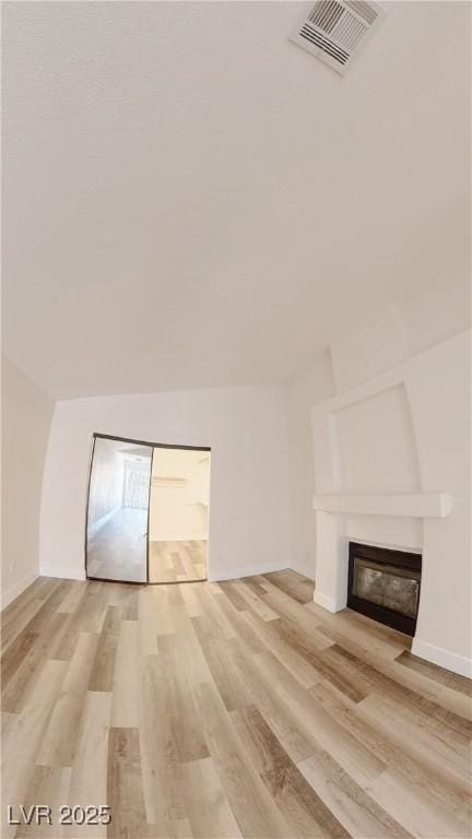 additional living space with light wood finished floors, a glass covered fireplace, visible vents, and baseboards