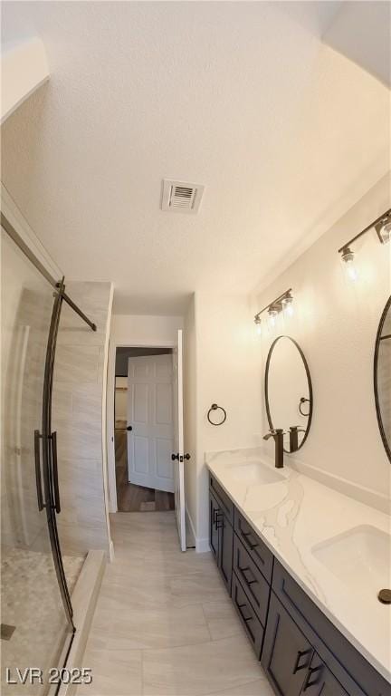 full bath with a stall shower, visible vents, a sink, and double vanity