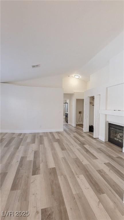 unfurnished living room with vaulted ceiling, visible vents, a glass covered fireplace, and light wood-style flooring