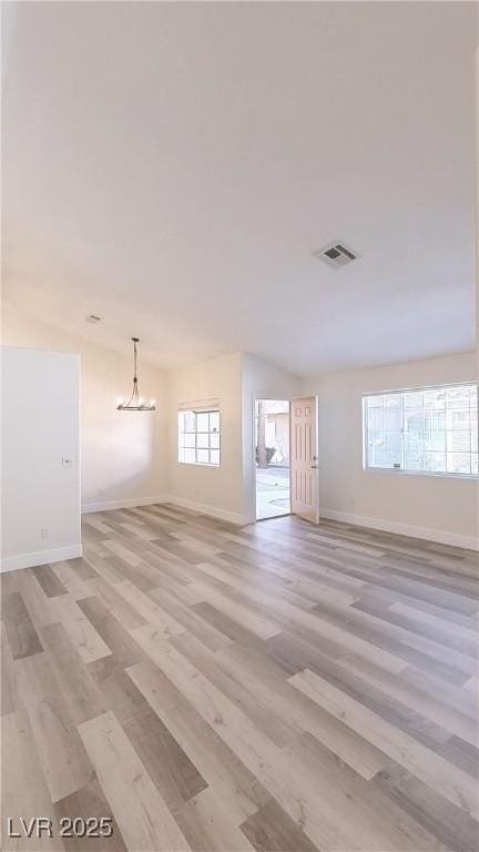 unfurnished room with light wood-style floors, lofted ceiling, visible vents, and baseboards