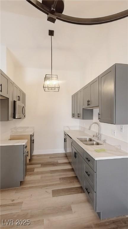 kitchen with light wood-style flooring, stainless steel microwave, light countertops, gray cabinetry, and a sink