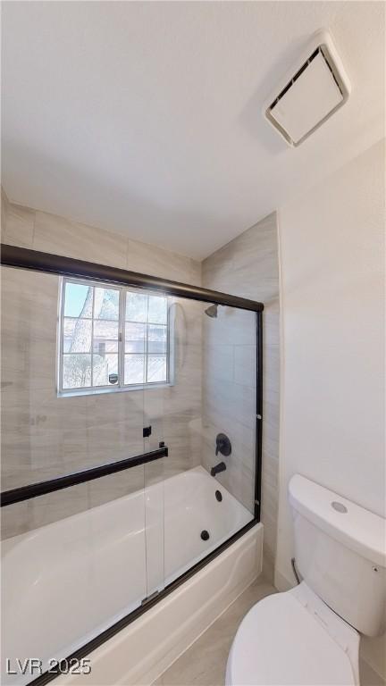 bathroom featuring toilet, bath / shower combo with glass door, and visible vents