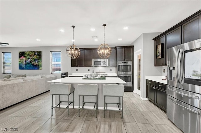 kitchen with stainless steel appliances, a breakfast bar, open floor plan, light countertops, and decorative light fixtures