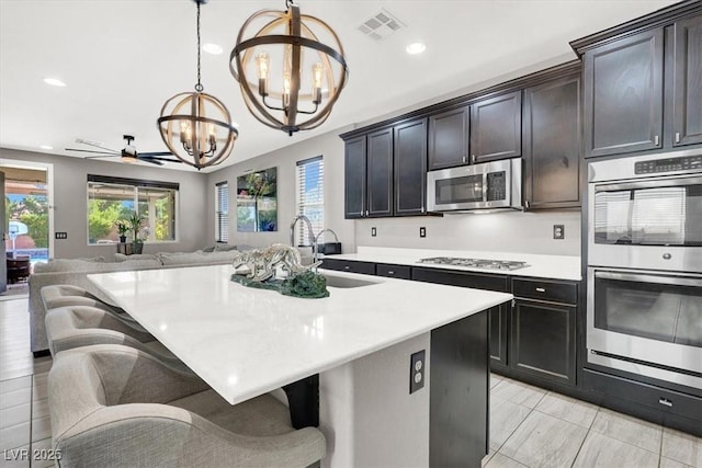 kitchen featuring stainless steel appliances, a sink, visible vents, open floor plan, and light countertops