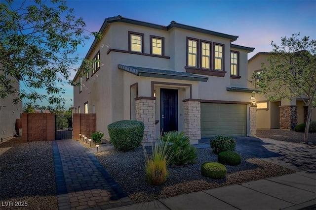 view of front of home with an attached garage, fence, decorative driveway, a gate, and stucco siding