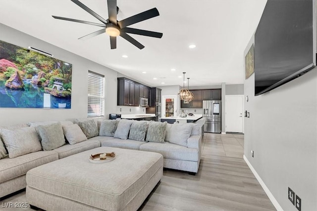 living room featuring recessed lighting, light wood finished floors, baseboards, and ceiling fan with notable chandelier