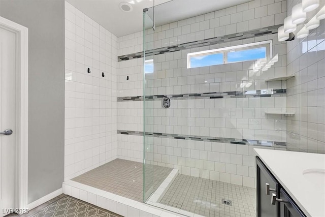 full bath featuring tile patterned flooring, baseboards, tiled shower, and vanity