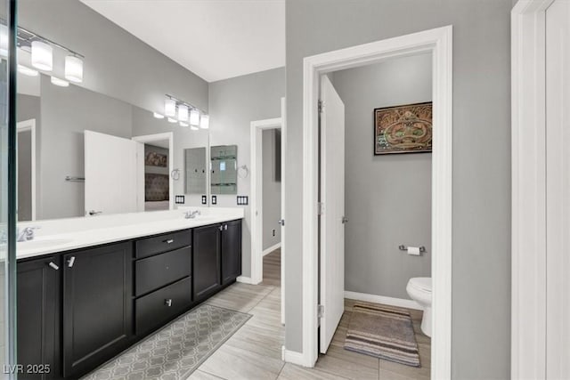 bathroom featuring baseboards, a sink, toilet, and double vanity