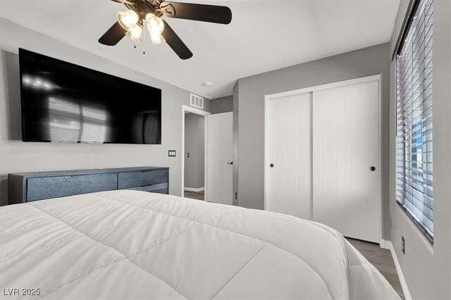 bedroom with baseboards, visible vents, ceiling fan, wood finished floors, and a closet