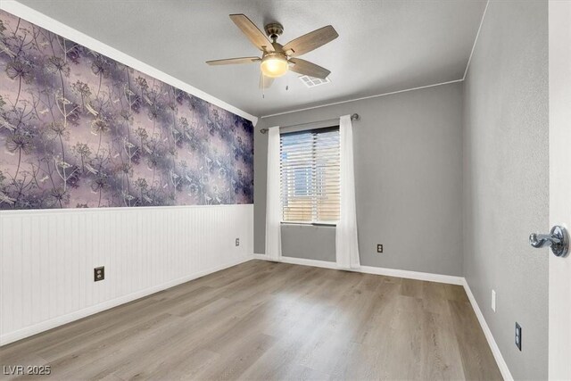 empty room with visible vents, a ceiling fan, wainscoting, wood finished floors, and baseboards