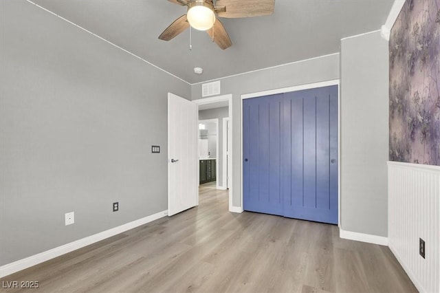 unfurnished bedroom with wood finished floors, visible vents, baseboards, a ceiling fan, and wainscoting