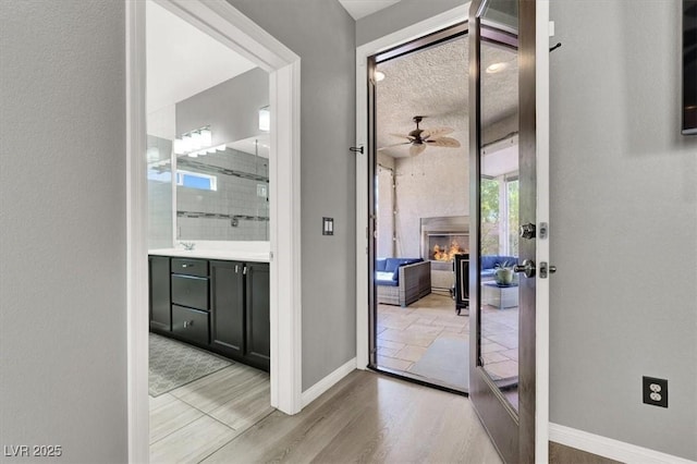 doorway featuring a warm lit fireplace, light wood-style flooring, baseboards, and ceiling fan