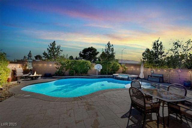 pool at dusk with a pool with connected hot tub, a fenced backyard, and a patio